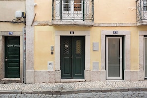 Ein Gebäude mit nummerierten Türen, einem Balkon und einer Kopfsteinpflasterstraße.