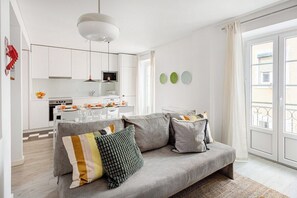 Ein modernes Wohnzimmer mit grauem Sofa, einem Esstisch mit Stühlen, einer Küchenzeile und einem Balkon mit Geländer.
