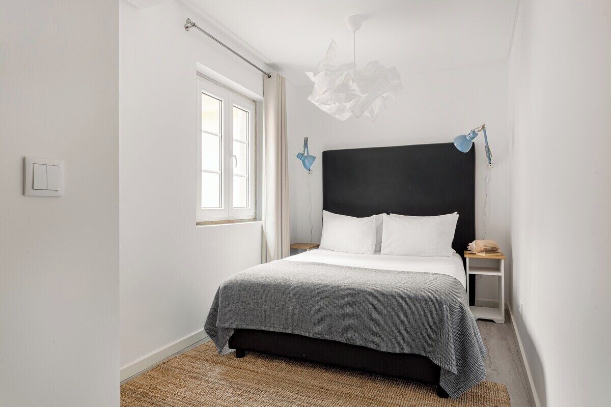 Un dormitorio con cama, mesita de noche, lámpara de pared e iluminación instalada en la pared.