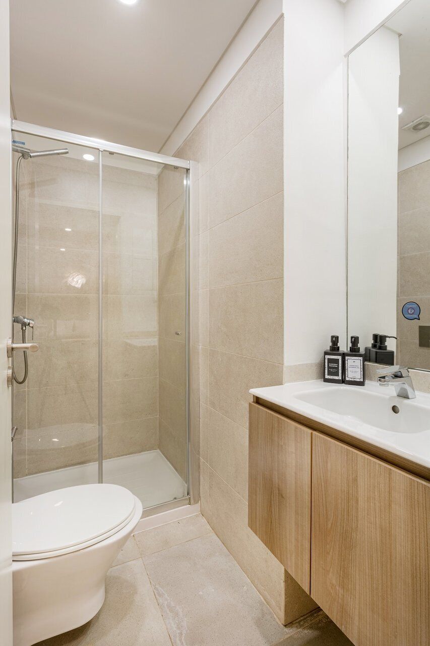 Une salle de bain moderne avec une douche à parois de verre, des toilettes blanches et un meuble-lavabo en bois avec un miroir.