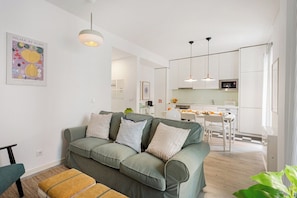 Ein modernes Wohnzimmer mit einem grünen Sofa, einem kleinen Tisch und einer Küche im Hintergrund.