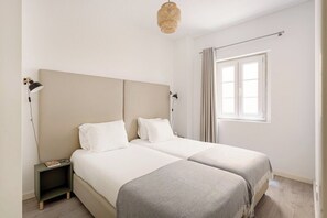 Ein Zimmer mit zwei Betten, einem Nachttisch, einer Lampe, einem Fenster mit Vorhängen und einer Hängelampe.