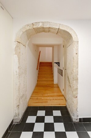 Ein Korridor mit Schachbrettboden, einer Holztreppe und einer gewölbten Tür.