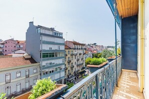 Ein Balkon mit Blick auf eine Stadtlandschaft, darunter mehrstöckige Gebäude und ein klarer Himmel.