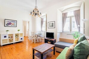 A living room with a wooden floor, a sofa, a TV, a dining table with chairs, and a chandelier. - Baixa-Chiado Getaway (Lisbon)