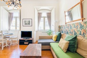 Ein Wohnzimmer mit Sofa, Fernseher, Esstisch, Stühlen und einer Chandelüster.