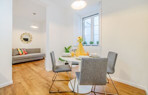 Ein Essbereich mit einem runden Tisch, vier grauen Stühlen, einer Vase mit gelben Blumen und einem Fenster mit Pflanzen auf dem Sims.