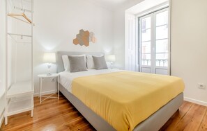 Ein Schlafzimmer mit Bett, Nachttischen, einem Kleiderhaken und einem Fenster.