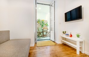 Ein Wohnzimmer mit einer Couch, einem an der Wand befestigten Fernseher und Holzboden.