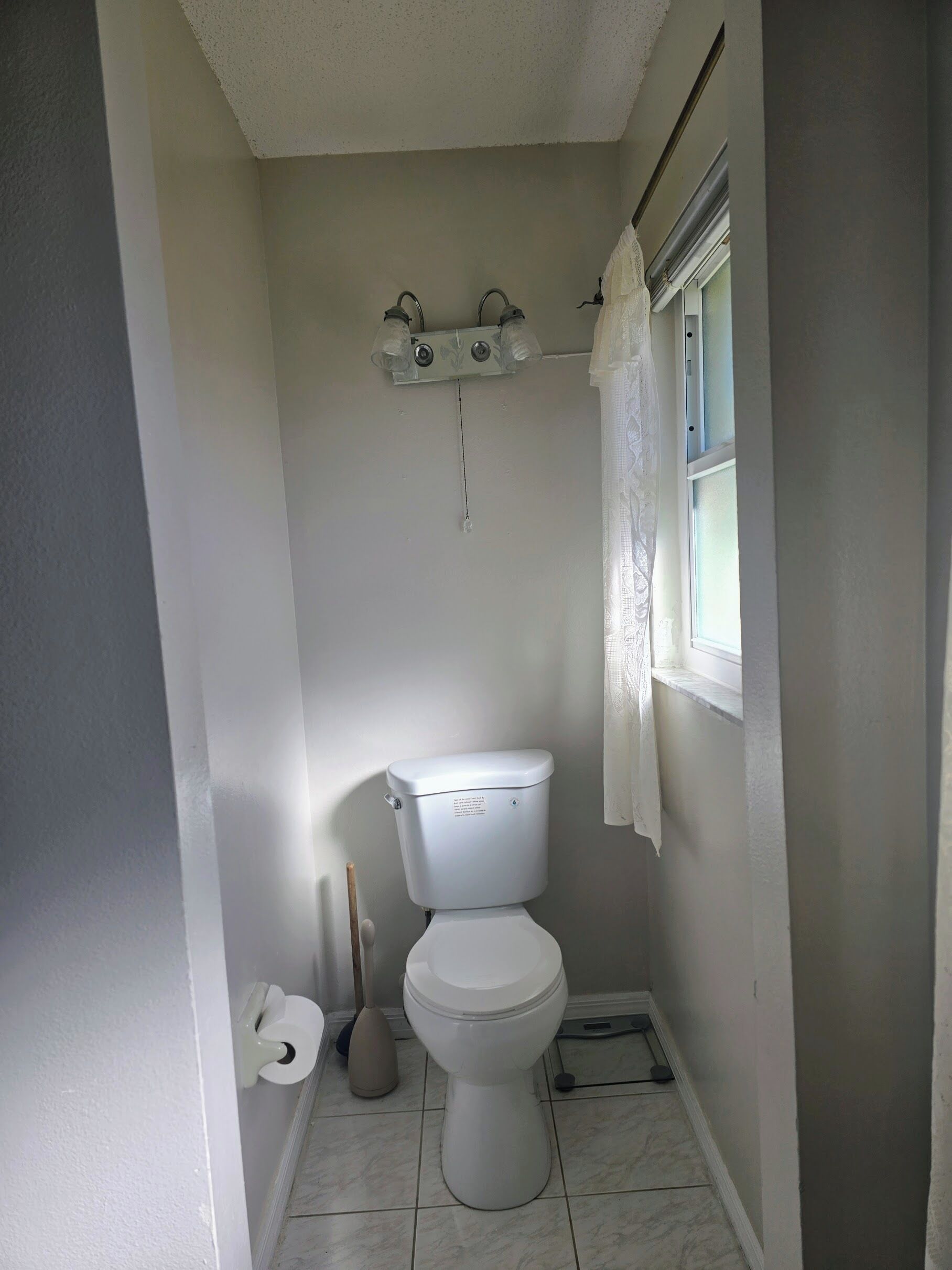 Une petite salle de bain propre, équipée de toilettes, d’un sèche-mains et d’une fenêtre avec un rideau.