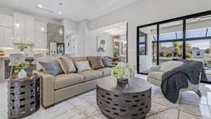 Ein modernes Wohnzimmer mit einem beigen Sofa, einem runden Couchtisch und einem großen Fenster mit Blick ins Freie.