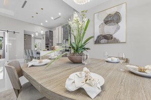 A modern dining area with a wooden table, chairs, and a potted plant. - Saltwater Pool, Game Room & Canal-View Escape - Gold Coast Getaway - Roelens (Cape Coral)