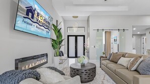 Ein modernes Wohnzimmer mit Kamin, großem Flachbildfernseher, Sofa und Couchtisch.