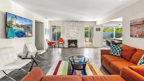 Amplia sala de estar con chimenea, muebles modernos y un televisor grande que muestra una escena de piscina.