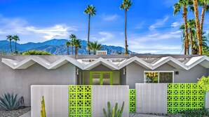 Una casa moderna con techo en zigzag, una puerta verde y vistas a las montañas.