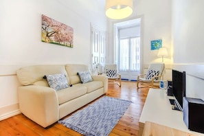 Ein Wohnzimmer mit einer Couch, einem Teppich, einem Fernseher und einem Bild an der Wand.