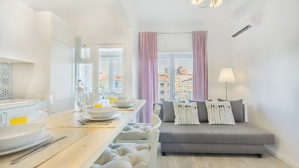 Ett modernt vardagsrum med en grå soffa, en matplats med ett träbord och utsikt genom stora fönster.