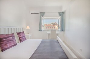 Ein Hotelzimmer mit Bett, Schreibtisch, einem Fenster mit Vorhängen und Blick auf Gebäude.
