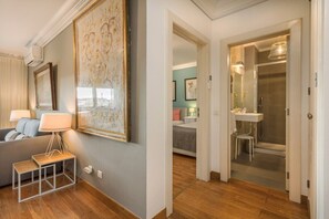 Ein modernes Interieur mit einer Couch, einer Lampe, einem gerahmten Kunstwerk und einem Badezimmer mit Dusche und Waschbecken.