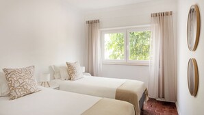 Ein Hotelzimmer mit zwei Betten, einem Fenster mit Vorhängen, einem Spiegel an der Wand und einem Holzboden.