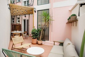 Eine gemütliche Terrasse mit einer Holzpergola, einem runden Tisch, Korbstühlen, einer Couch und Topfpflanzen.