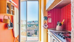 Une cuisine avec un mur recouvert de carreaux rouges, une cuisinière à gaz et une porte vitrée donnant sur l’extérieur.