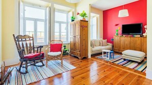 Un salon avec un plancher en bois, un fauteuil à bascule, un canapé, une télévision et un mur rouge.