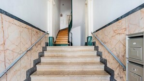 Un escalier en marbre, doté d’une main courante en bois et de balustres en métal, mène à un palier où se trouve une porte et un autre escalier avec une rampe verte.