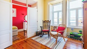 Une pièce avec un plancher en bois, un mur rouge, une armoire blanche, une chaise en bois, une petite table verte et une fenêtre donnant sur un beau paysage.