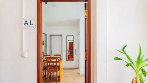 Un couloir avec un plancher en bois, un coin repas avec des chaises et une table, et une plante sur la droite.