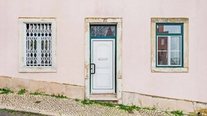 Un bâtiment avec une porte blanche, une fenêtre dotée d’une grille métallique et une autre fenêtre avec un cadre vert.