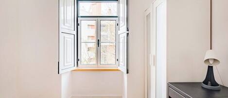 A room with a large window, a bed, a desk, and a cabinet.