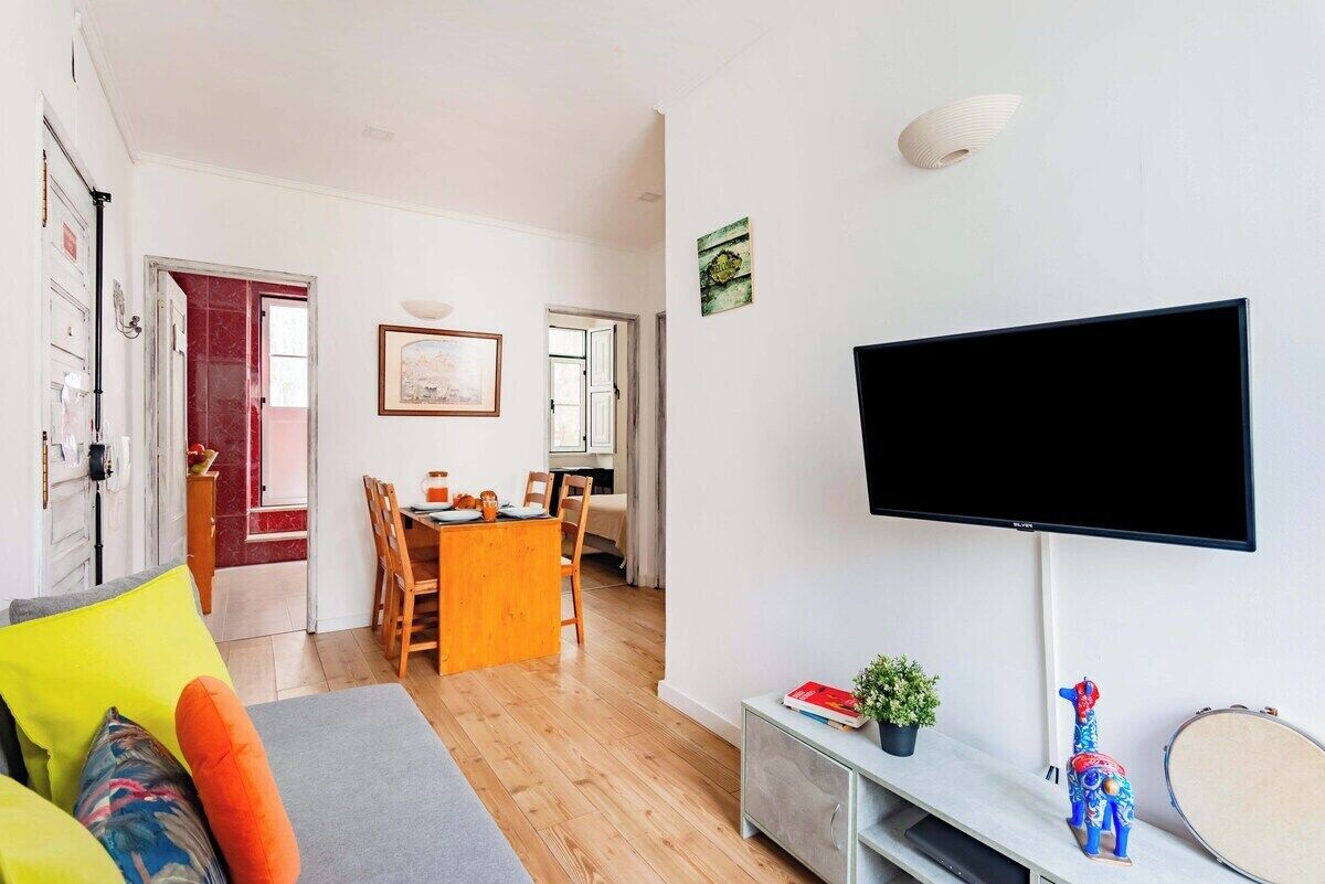 A living room with a TV, a dining area, and a kitchen visible through an open door.