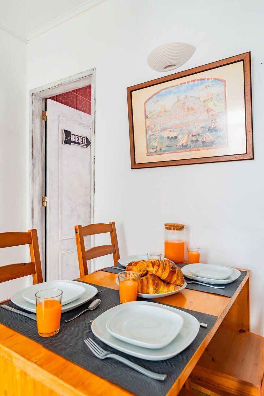 A breakfast table set with plates, croissants, and orange juice, a door with a beer sign, and a framed picture on the wall.