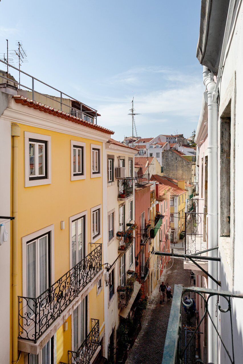 Une rue étroite, bordée de bâtiments des deux côtés, avec des balcons dotés de balustrades et un ciel dégagé.