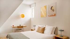 Ein Schlafzimmer mit Bett, Nachttischen, einem Schreibtisch, einem Stuhl und Bildern an der Wand.