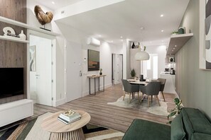 Ein modernes Wohnzimmer mit Fernseher, Sitzgelegenheiten, einer Essecke und einer Küche.
