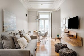Ein modernes Wohnzimmer mit Sofa, Esstisch und Stühlen, einem an der Wand montierten Fernseher und einem Balkon mit Aussicht.