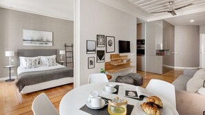 A modern hotel room with a bed, a dining table with breakfast, a TV, and a kitchen area. - Trendy Flat in the iconic Chiado (Lisbon)