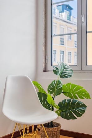 Ein weißer Stuhl, ein Topf mit einem Monstera-Farn und ein Fenster mit Blick auf Gebäude.