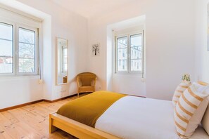 Ein Schlafzimmer mit Bett, zwei Fenstern, einem Sessel und einem Wandbild.