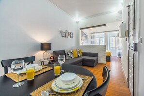 Ein Essbereich mit einem runden Tisch, gedeckt für zwei Personen, einer Couch im Hintergrund und Blick ins Wohnzimmer.