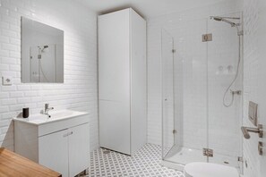 A modern bathroom with a white tiled wall, a glass shower enclosure, a white sink, and a wooden countertop. - Lisbon City Vibes, 2BR Flat (Lisbon)