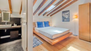 Ein Schlafzimmer mit geneigter Decke, einem Bett mit blauen Kissen, einer Nachttischlampe und einem Gemälde an der Wand.