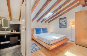 Ein Schlafzimmer mit geneigter Decke, einem Bett mit blauen Kissen, einer Nachttischlampe und einem Gemälde an der Wand.