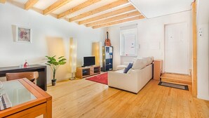 Ein Wohnzimmer mit Holzbalkendecke, einer Couch, einem Fernseher, einer Gitarre und einem Esstisch.