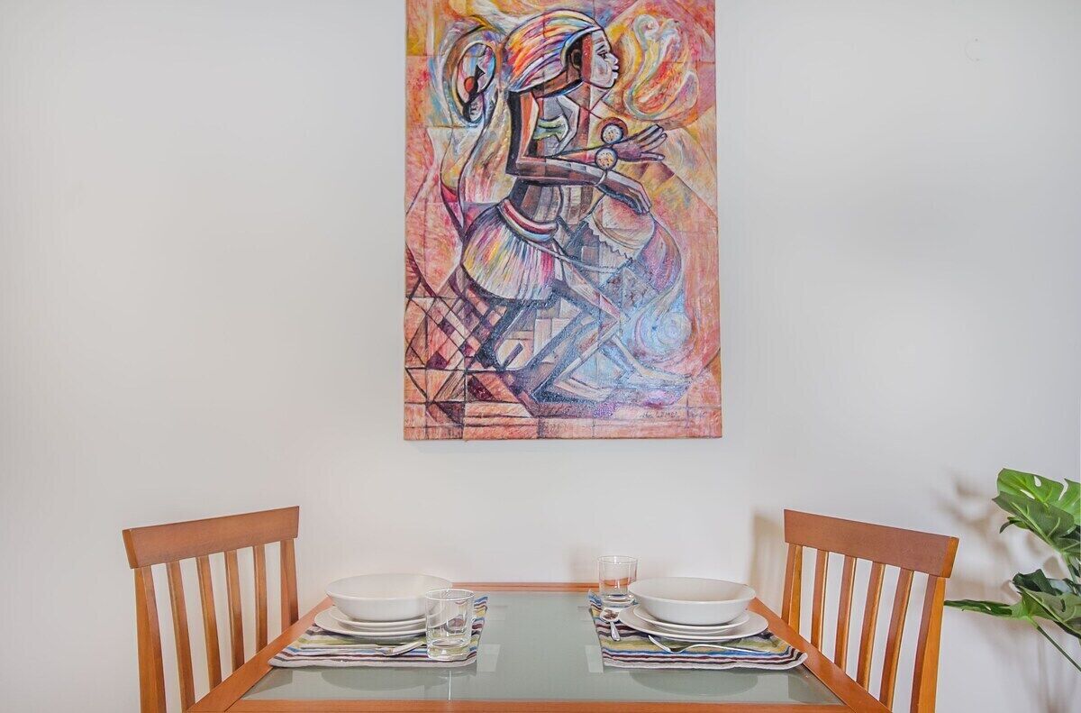 Een eettafel met stoelen, een glazen blad en een schilderij aan de muur.