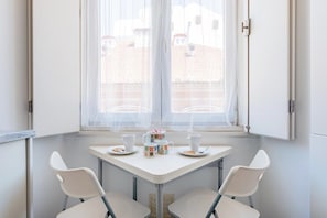Ein kleiner Raum mit Fenster, einem Tisch mit zwei Stühlen und einem Kaffeegedeck auf dem Tisch.