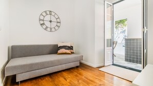 A room with a grey sofa, a wall clock, and a sliding glass door leading to an outdoor area. - Olarias Terrace Lisbon III (Lisbon)