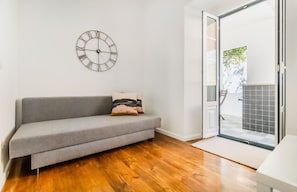 A room with a grey sofa, a wall clock, and a sliding glass door leading to an outdoor area. - Olarias Terrace Lisbon III (Lisbon)